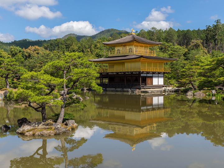 The gold-covered Kinkaku-ji pavilion reflected in a calm pond surrounded by pines